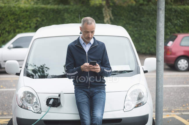 Homem usando telefone celular ao carregar carro elétrico na estação de carregamento — Fotografia de Stock