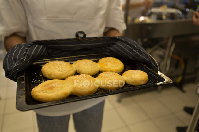 Section du milieu du chef tenant plateau de biscuits dans la cuisine — Photo de stock
