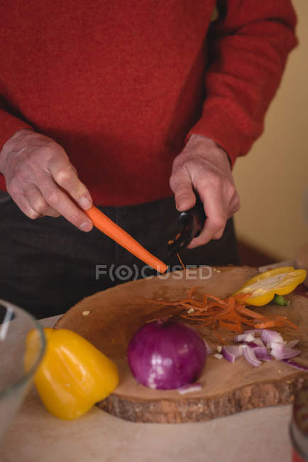 Seniorin schneidet Karotte mit Messer in Küche — Stockfoto