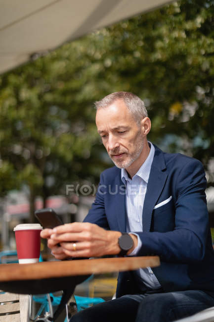 Uomo d'affari che utilizza il telefono cellulare in un bar all'aperto in una giornata di sole — Foto stock