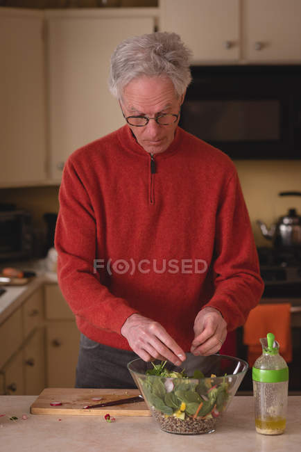 Homem sênior preparando salada na cozinha em casa — Fotografia de Stock