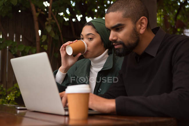 Pareja romántica usando portátil mientras toma café en la cafetería - foto de stock