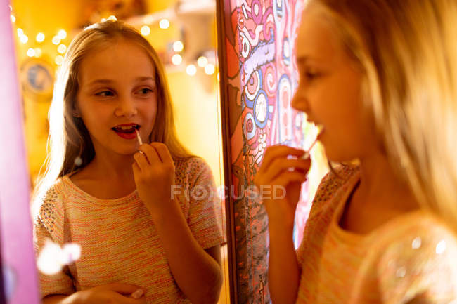 Chica sonriente mirando en el espejo y aplicando lápiz labial rojo - foto de stock