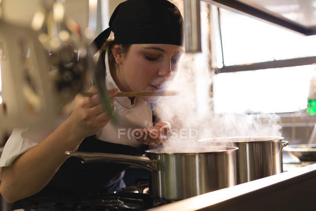 Female chef tasting food in kitchen at restaurant — Stock Photo