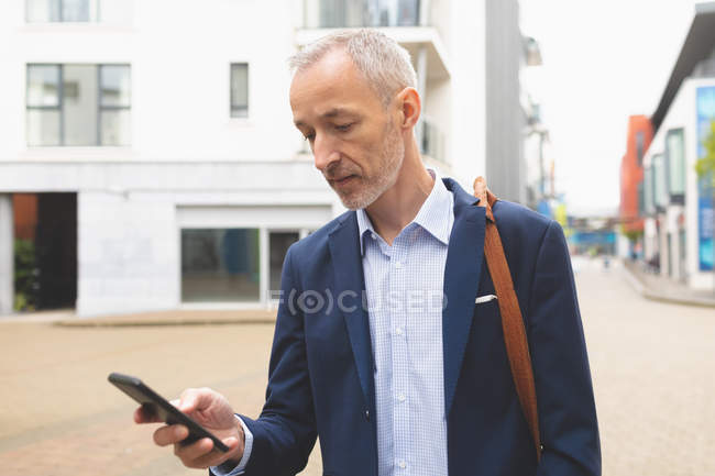 Empresario usando teléfono móvil en la ciudad en un día soleado - foto de stock