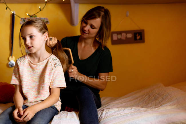 Мать расчесывает дочерей волосы на кровати дома — стоковое фото