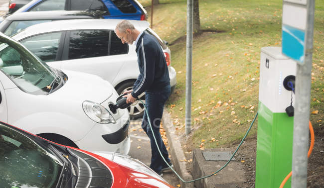 Vue latérale de l'homme rechargeant la voiture électrique à la station de charge — Photo de stock