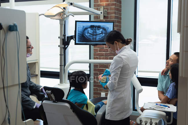 Dentista femenina explicando sobre modelo de dientes en clínica - foto de stock