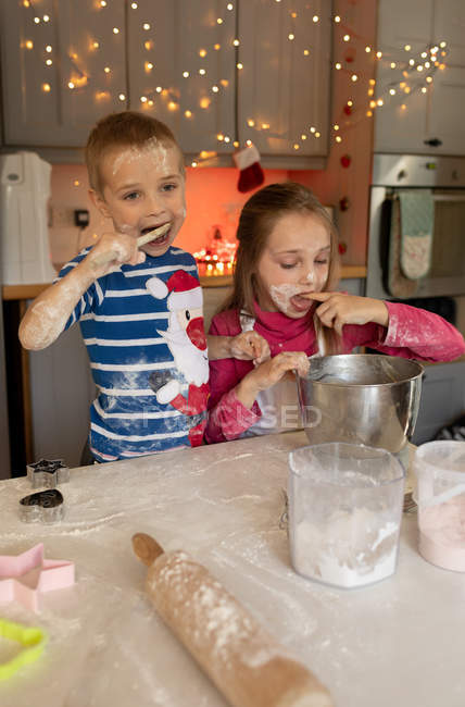 Irmãos degustando a massa para biscoitos de Natal na cozinha — Fotografia de Stock