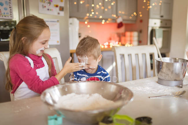 Hermanos sonrientes jugando con harina en la cocina - foto de stock