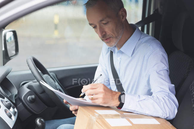 Vista lateral do homem da entrega que escreve no papel na van da entrega — Fotografia de Stock