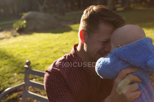Отец держит своего малыша в парке в солнечный день — стоковое фото