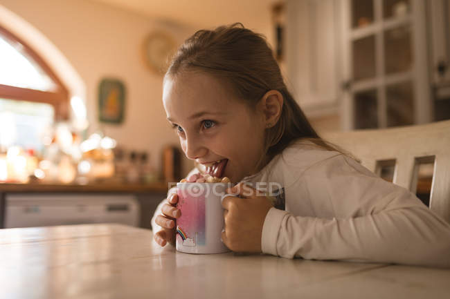 Sorridente ragazza leccare il biscotto sulla tazza — Foto stock