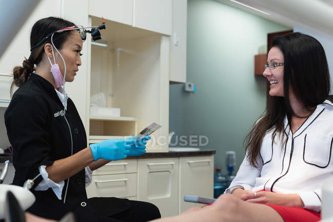 Dentista que interactúa con una paciente en una clínica dental - foto de stock