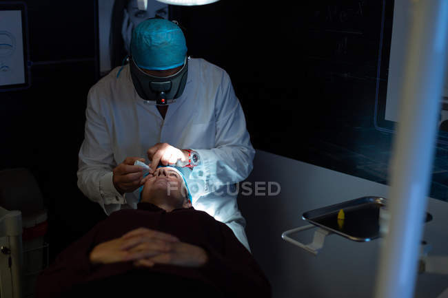 Оптометрист осматривает глаза пациента с помощью оборудования для проверки зрения в клинике — стоковое фото