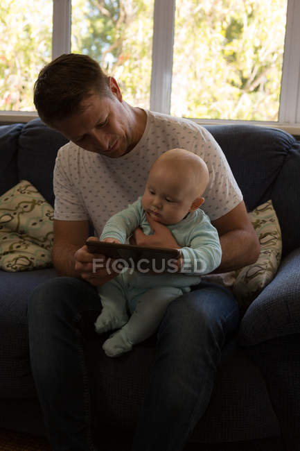 Padre y bebé niño usando tableta digital en la sala de estar en casa - foto de stock