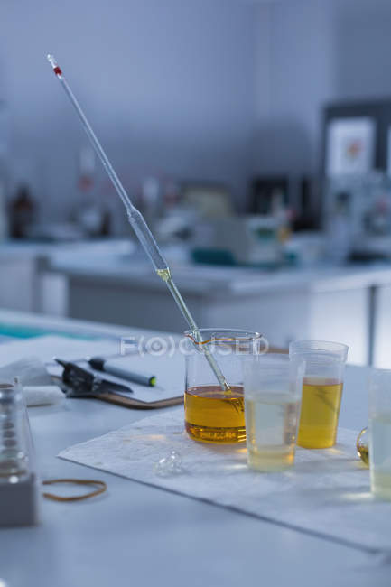 Beaker, pipeta volumétrica e prancheta na mesa em laboratório — Fotografia de Stock