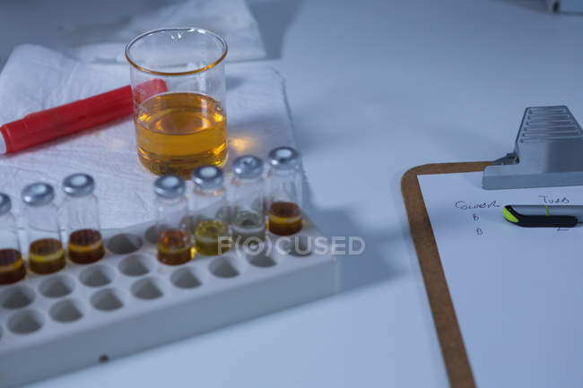 Close-up of beaker, test tube rack and clipboard on table — Stock Photo