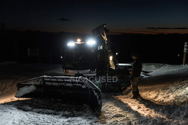 Mann steht nachts neben Schneepflug-Maschine — Stockfoto