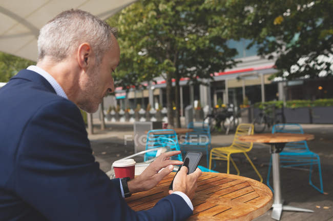 Вид збоку бізнесмена, що використовує мобільний телефон у відкритому кафе — стокове фото