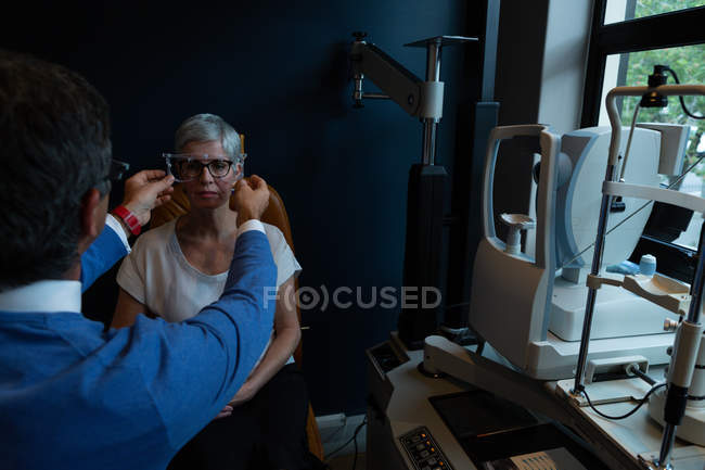 Optometrist examining patient eyes with eye test equipment in clinic — Stock Photo