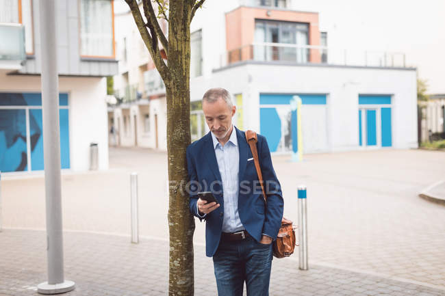 Бизнесмен, использующий мобильный телефон в городе в солнечный день — стоковое фото