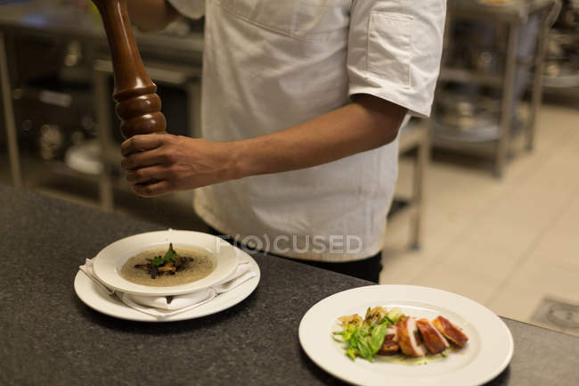 Sección media del chef usando molino de pimienta en la cocina del restaurante - foto de stock