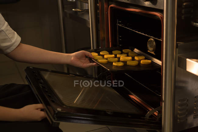 Chef poniendo bandeja de galletas en el horno en el restaurante - foto de stock