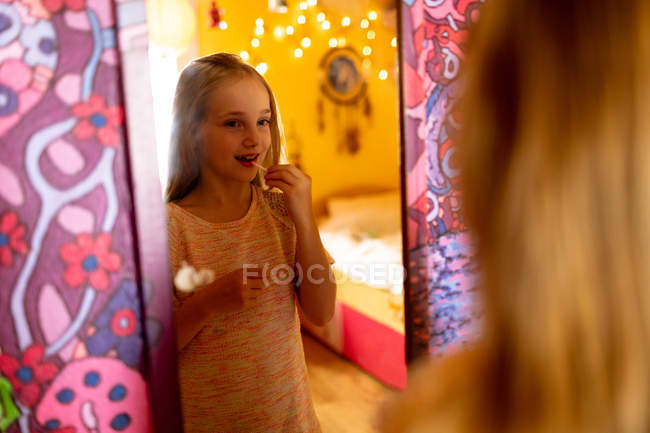 Menina adorável olhando no espelho e aplicando batom vermelho — Fotografia de Stock