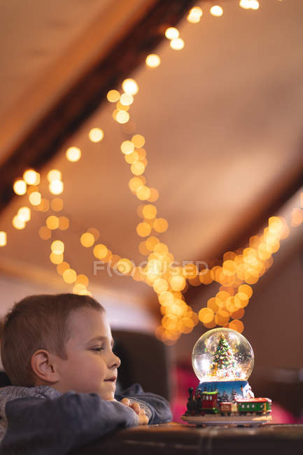 Menino olhando para árvore de Natal globo de neve em casa — Fotografia de Stock