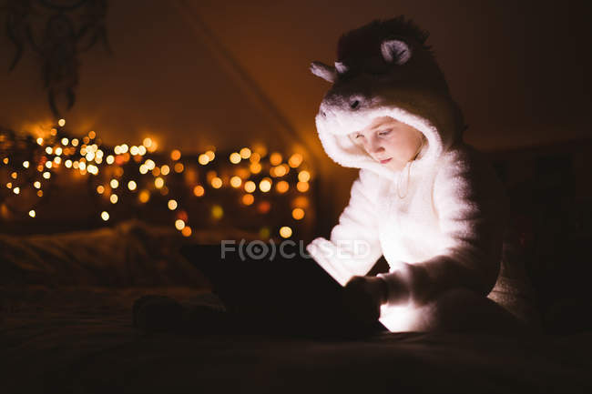Girl in hooded jacket using digital tablet against Christmas lights — Stock Photo