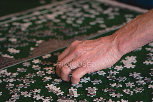 Primer plano del hombre mayor jugando juego de puzzle en casa - foto de stock