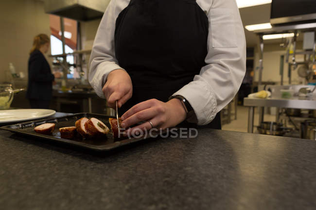 Mid section of chef cutting bacon with knife in restaurant — Stock Photo