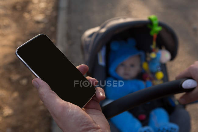 Vater benutzt Handy mit Baby im Kinderwagen im Park — Stockfoto