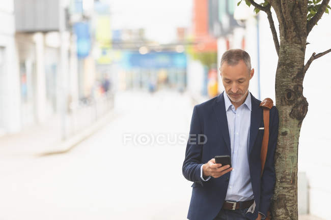 Empresário usando telefone celular na cidade em um dia ensolarado — Fotografia de Stock