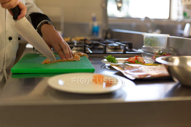Sección media del chef cortando carne en la tabla de cortar en la cocina - foto de stock