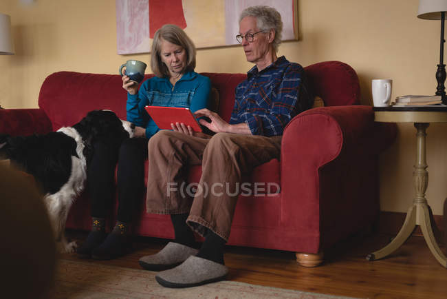 Senioren-Paar nutzt digitales Tablet beim Kaffee im heimischen Wohnzimmer — Stockfoto
