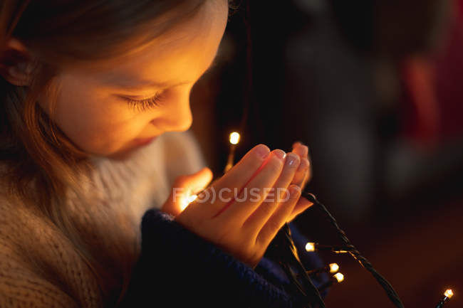Primo piano della ragazza guardando le luci delle fate illuminate a casa — Foto stock