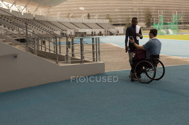 Dos atletismo discapacitados discutiendo por teléfono móvil en el lugar de deportes - foto de stock