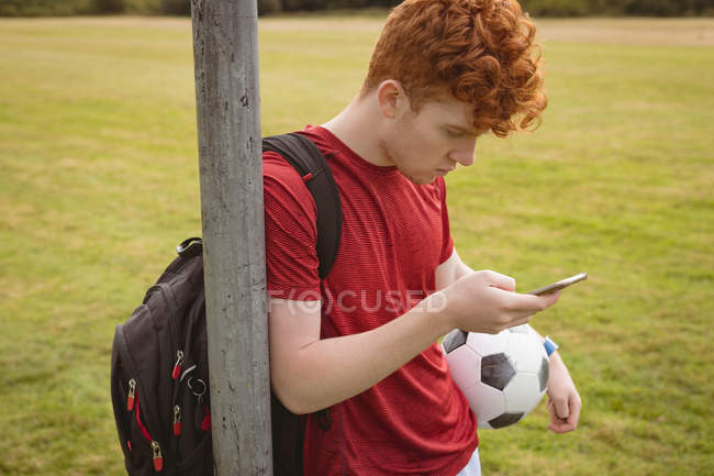 Giovane giocatore di calcio che utilizza il telefono cellulare sul campo — Foto stock