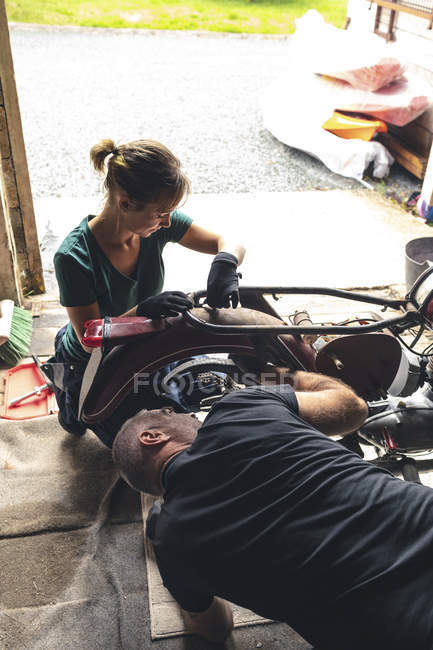 Mecanicistas masculinos e femininos reparando moto na garagem de reparação — Fotografia de Stock
