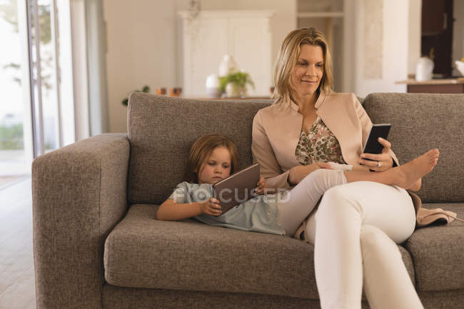 Мати і дочка використовують цифровий планшет і мобільний телефон у вітальні вдома — стокове фото