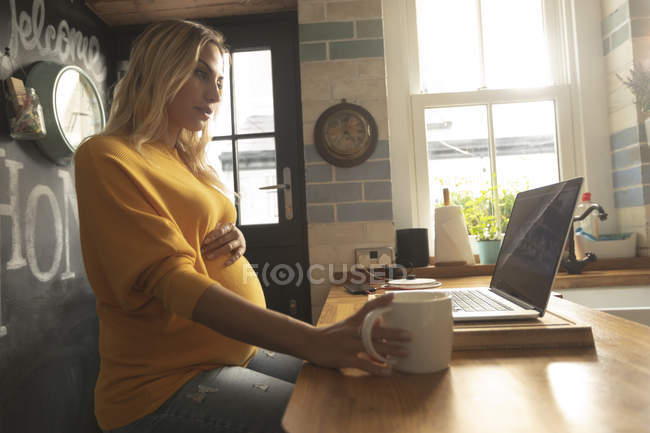 Концентрована вагітна жінка використовує ноутбук вдома — стокове фото