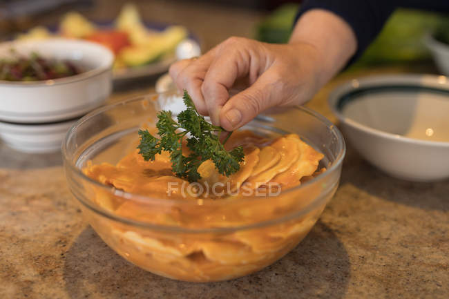 Gros plan de la femme garnissant la coriandre sur la nourriture dans la cuisine — Photo de stock