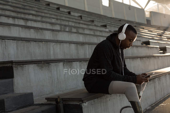 Спортсмен з обмеженими можливостями слухає музику на мобільному телефоні на спортивному майданчику — стокове фото
