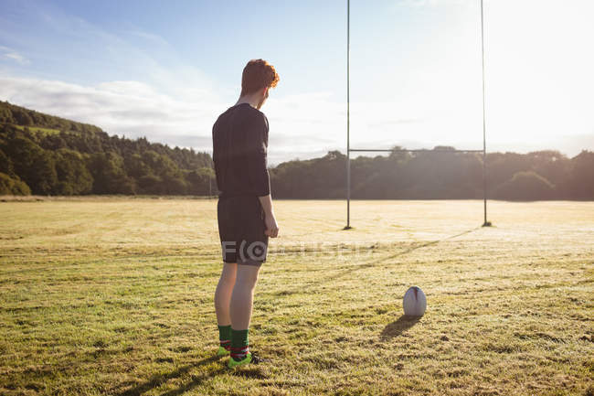 Jugador de rugby de pie con pelota de rugby en el campo en un día soleado - foto de stock