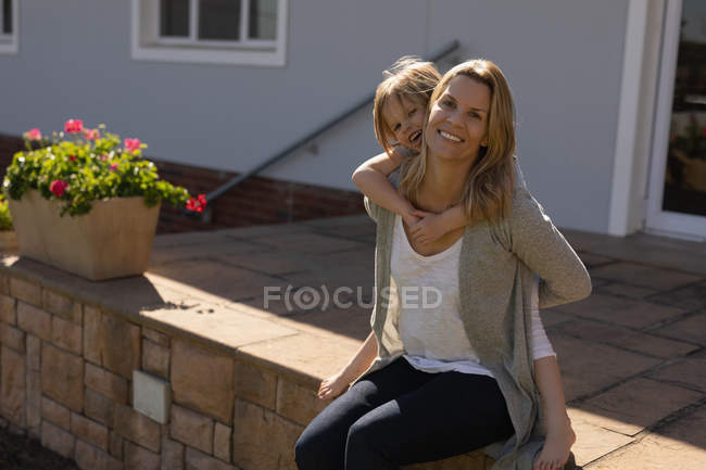 Mère heureuse donnant le tour de piggyback à sa fille dans le porche — Photo de stock