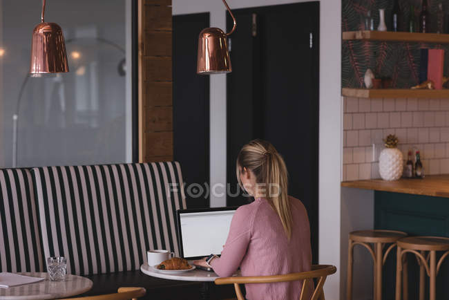 Rear view of businesswoman working on laptop in cafeteria at office — Stock Photo