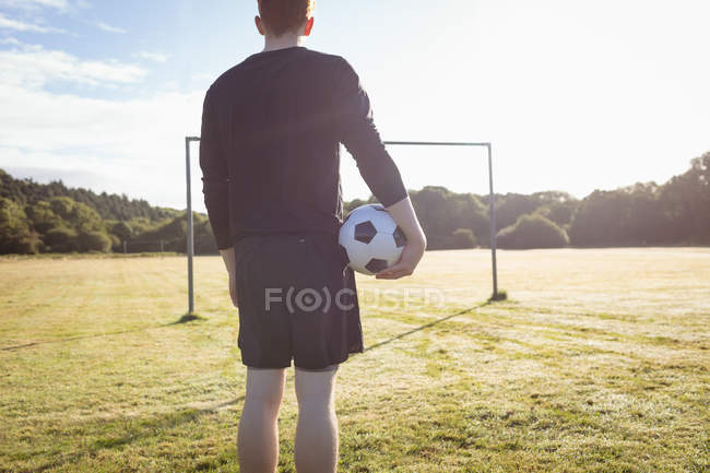 Vista trasera del jugador de fútbol de pie con pelota de fútbol en el campo - foto de stock
