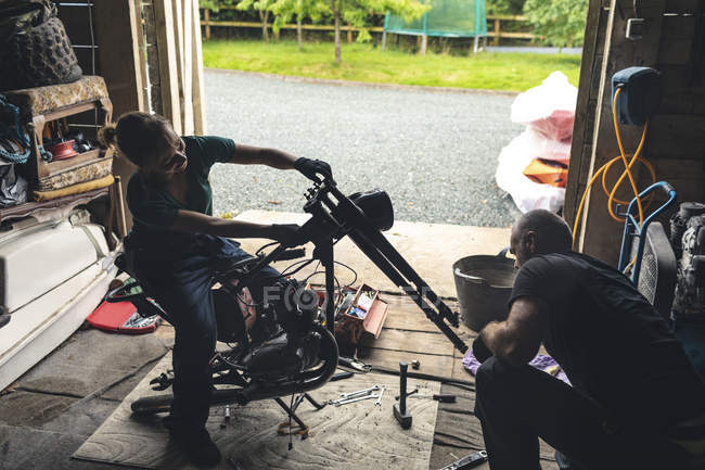 Male and female mechanicians repairing motorbike in repair garage — Stock Photo
